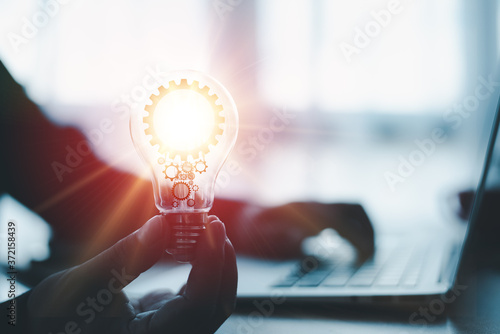 The hand of a man with a light bulb And there is a gear icon in it And he is using a notebook computer. The idea of ​​inspiration from online technology.innovation idea concept.