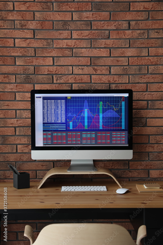Fototapeta premium Modern computer with statistic information on wooden table near brick wall