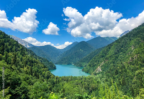 Blue lake of Abkhazia, high in the mountains, among greenery. Blue sky with white clouds.