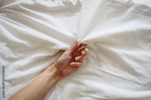 Close up sexy woman hand pulling and squeezing white sheets in ecstasy in bed. Orgasm on white bed. Sex and erotic concept.