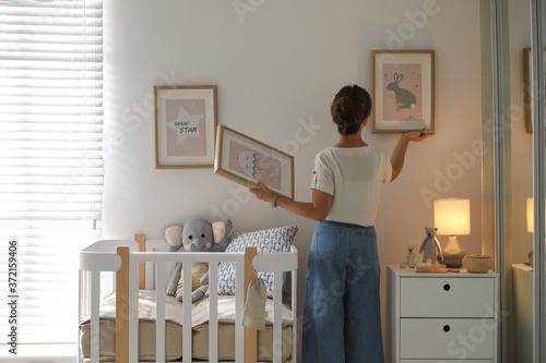 Decorator hanging pictures on wall in baby room. Interior design