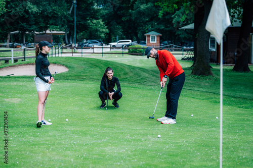 Photo Golf putting lesson, two young female golfers practicing putting with golf instr