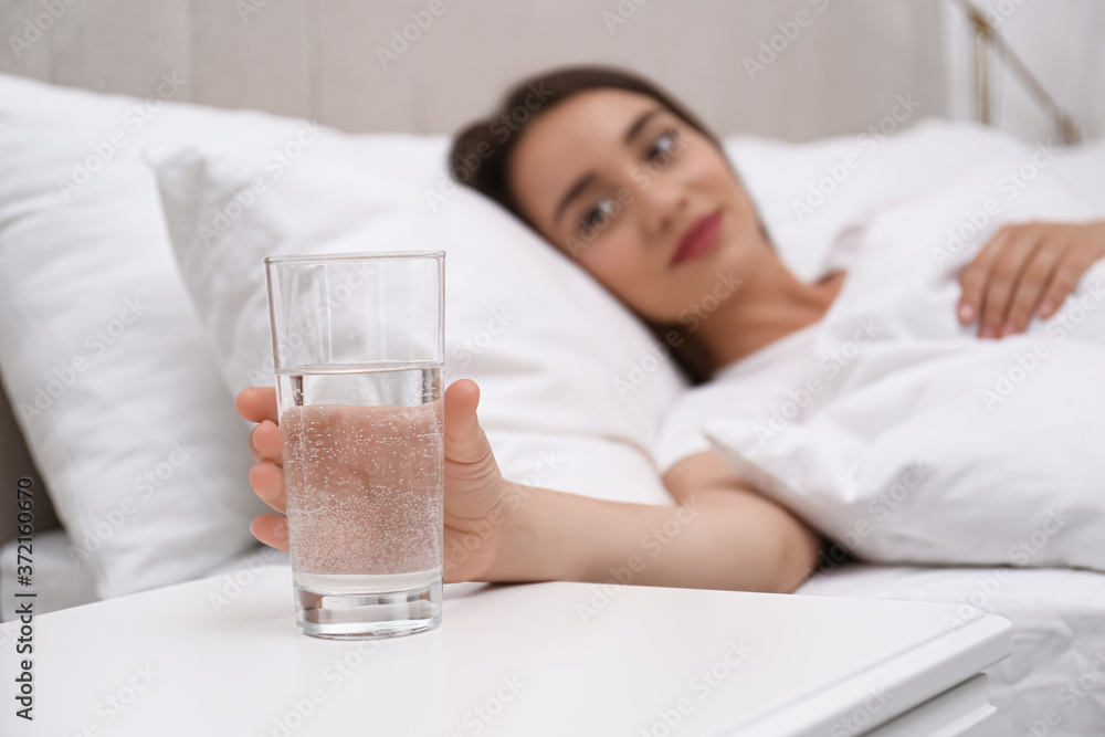 Young woman taking glass of water from nightstand at home, focus on hand Young woman taking glass of water from nightstand at home, focus on hand