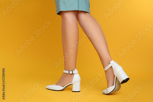Woman wearing stylish shoes on yellow background, closeup