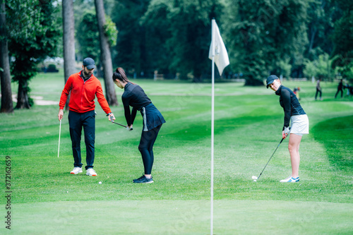Two young golfers practicing chipping shots on a golf course with golf instructor
