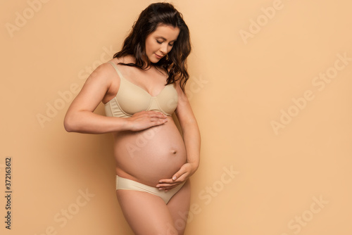  pregnant woman in underwear touching belly on beige