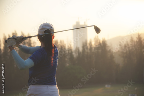 Female golfer or asian woman golf player doing golf swing tee off on the green sunset evening time, she presumably does exercise.