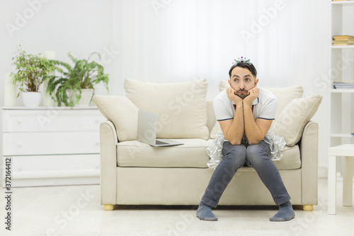 Young single father overwhelmed with household chores sitting on sofa in living room.