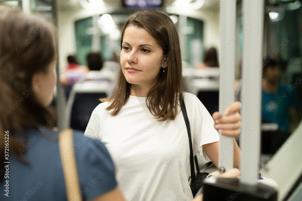 Fototapeta premium Young attractive brunette talking friendly with her fellow traveler on way to work by bus or tram in early morning