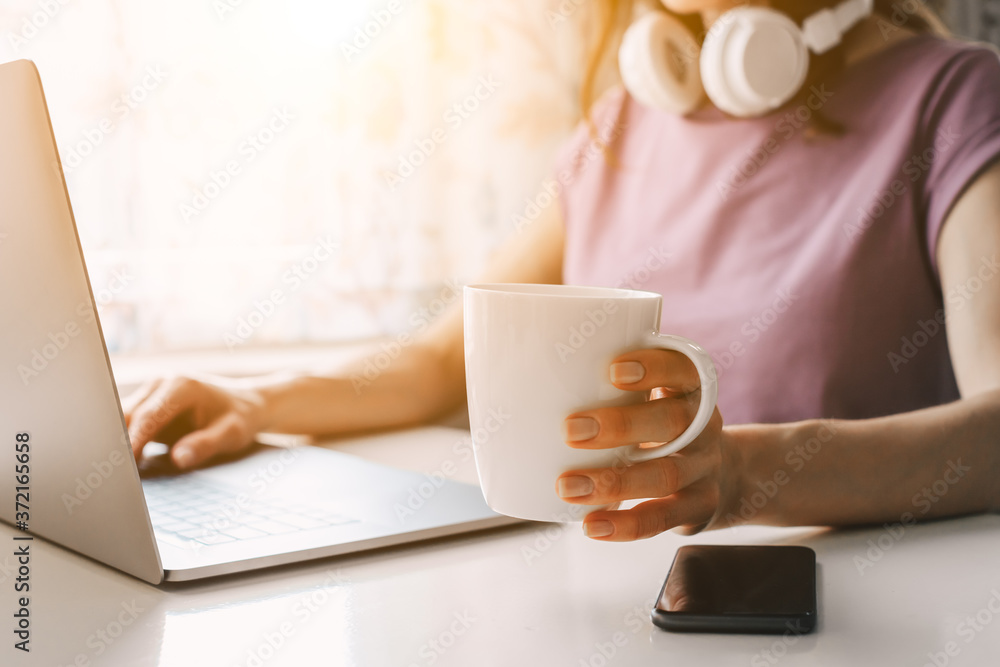 Cropped image of a young woman working at the laptop and drinking coffee. A girl holding white mug, mockup (template) cup for designs (focus on cup). Cropped image of a young woman working at the laptop and drinking coffee. A girl holding white mug, mockup (template) cup for designs (focus on cup).
