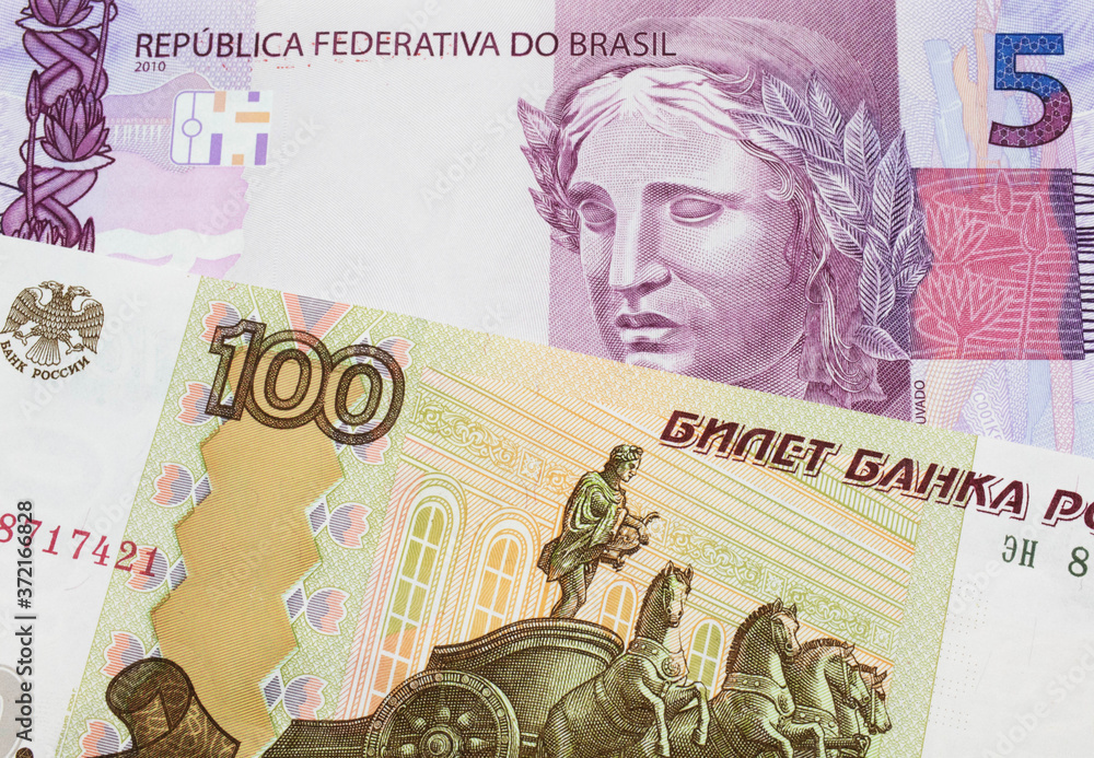 Fototapeta premium A macro image of a Russian one hundred ruble note paired up with a pink and purple five real bank note from Brazil. Shot close up in macro.