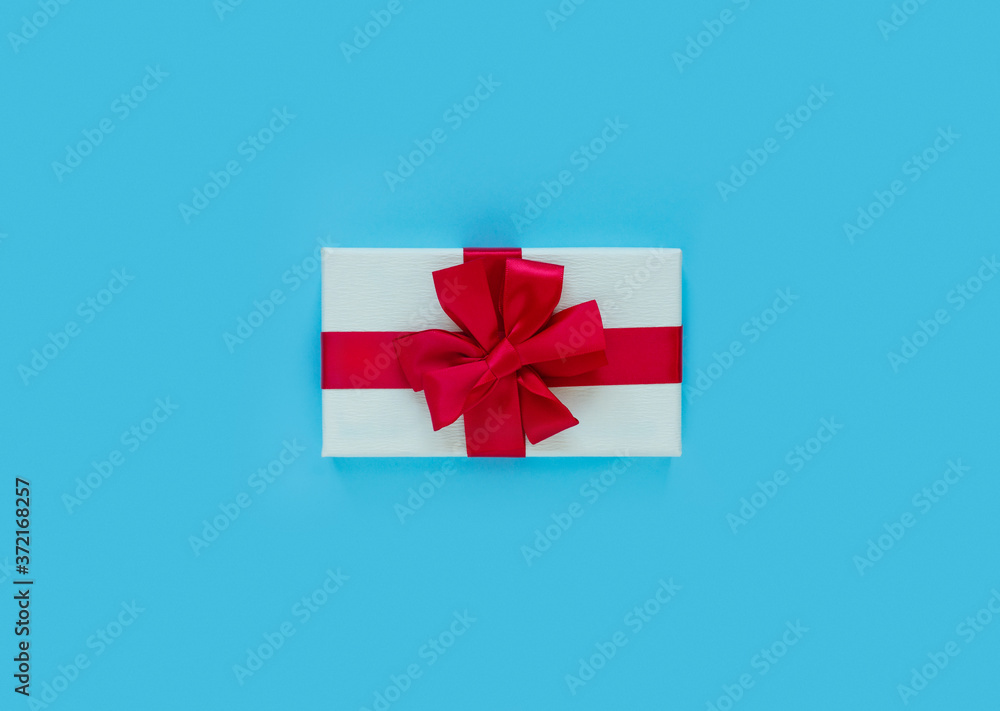 Fototapeta premium Pink gift box with red bow and ribbon on blue paper background with empty place for text.