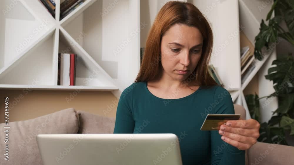 Pretty girl is making online payment holding bank card using modern laptop at home sitting on sofa. Finance, shopping in internet and youth concept. Pretty girl is making online payment holding bank card using modern laptop at home sitting on sofa. Finance, shopping in internet and youth concept.