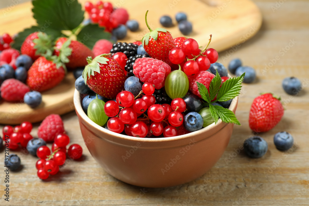 Mix of different fresh berries in bowl on wooden table Mix of different fresh berries in bowl on wooden table