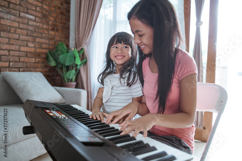 two sisters enjoy playing the piano at home doing activities during the pandemic in the family room background