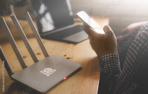 closeup of a wireless router with wifi 6 technology and a man using smartphone on living room at home ofiice