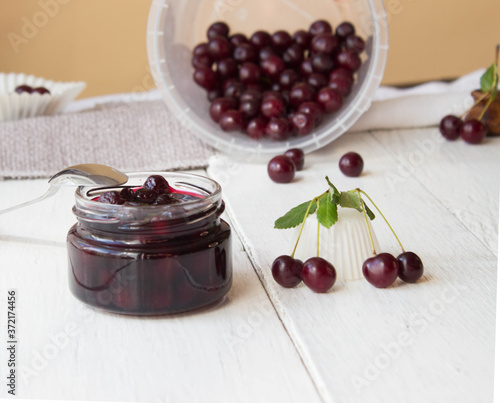 Glass jar with cherry jam on the white wooden boards on background of  fresh cherry
