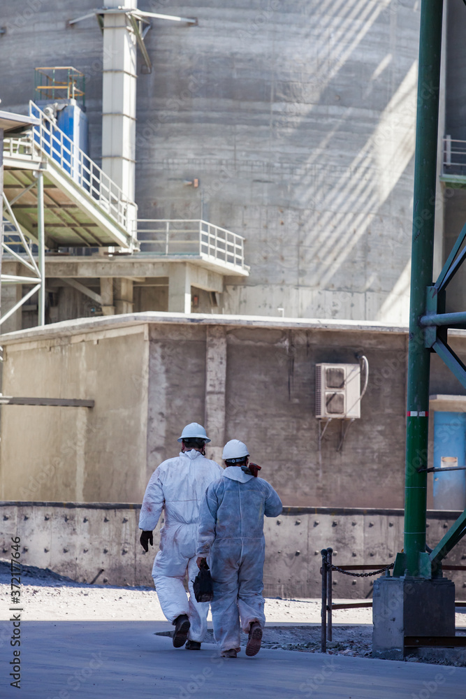 Two engineers (workers) in white helmets and white protective suits with tools. On grey concrete industrial building wall with shadows background. Two engineers (workers) in white helmets and white protective suits with tools. On grey concrete industrial building wall with shadows background.