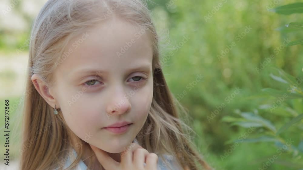 A beautiful girl stands by the green bushes. Portrait of a little girl. A beautiful girl stands by the green bushes. Portrait of a little girl.
