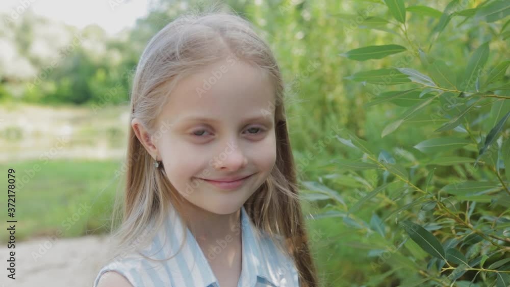 A beautiful girl stands by the green bushes. Portrait of a little girl. A beautiful girl stands by the green bushes. Portrait of a little girl.