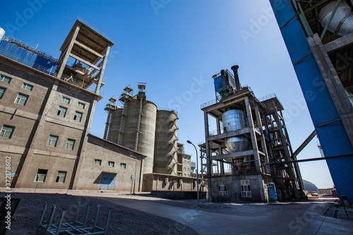 Mynaral, Kazakhstan: Grey loader hoppers, mixing towers, silos and industrial building of Jambyl Cement plant. Wide-angle panoramic view.