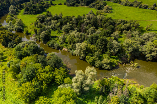 a panoramic view from a drone of a dark river and green trees around in summer