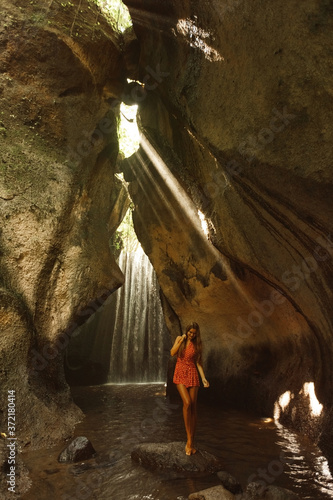 Young woman traveller in Bali stand in the cave in front of famous waterfal Tukad Cepung. Travel Indonesia concept