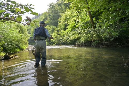 fly fisherman in summer fishing in a mountain river with waders and a cap