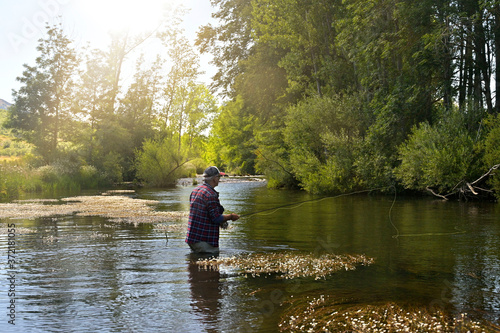 fly fisherman in summer fishing in a mountain river with waders and a cap