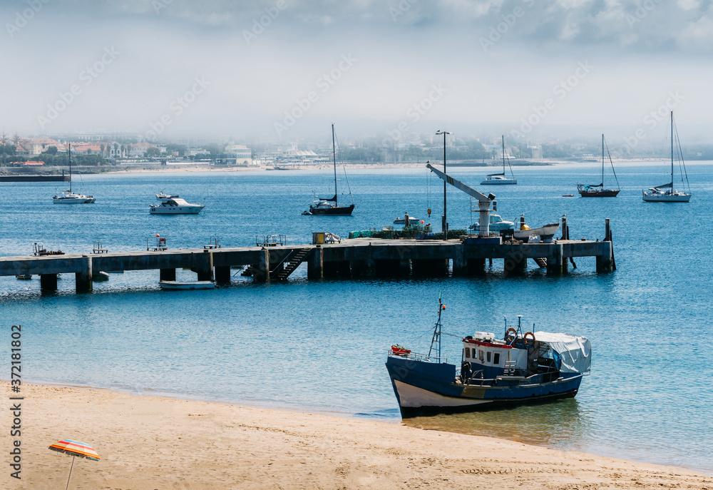 Wooden fishing boat moored on empty Ribeira beach in Cascais, Portugal with scenic background