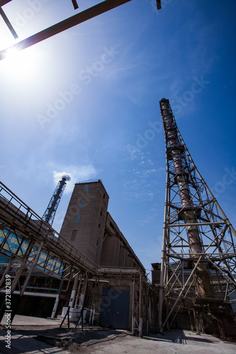 Smoking plant chimney and pipelines and industrial building of chemical factory on blue sky. Phosphoric fertilizers plant.