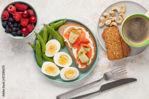 Healthy breakfast -  open sandwich with salmon and cucumber  boiled eggs  peas  coffee  biscuits  nuts and berries on a bright background. Top view.