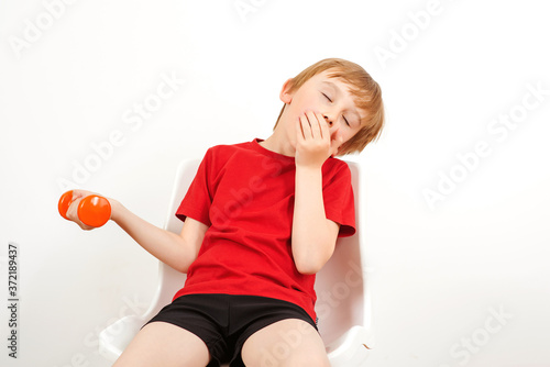 Tired kid after workout with dumbbells. Boy resting and sitting on the chair. Kids fittnes. Healthy childhood. photo