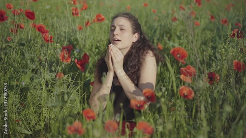 Portrait of young woman sitting in field of poppies and sneezing. Brunette Caucasian allergic lady on green flower lawn in sunlight. Ill woman outdoors on sunny summer day. photo