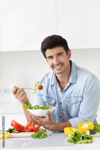 Handsome smiling young man with plate of salad fresh vegetables looking at camera.
