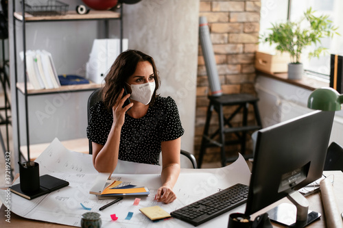 Beautiful businesswoman with medical mask working in office. Young businesswoman uing the phone.. photo