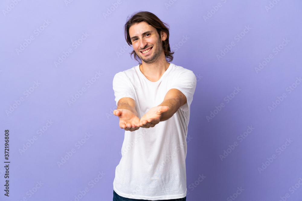 Young handsome man isolated on purple background holding copyspace imaginary on the palm to insert an ad Young handsome man isolated on purple background holding copyspace imaginary on the palm to insert an ad