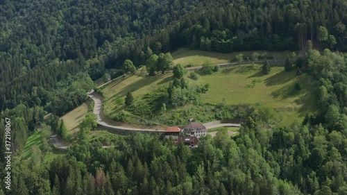 Aerial shot of mountain road a valley at the blackwood schwarzwald with fir wood forest witrh a house Roadhouse rest house on a sunny summer day gernany panorama rotation drone shot photo