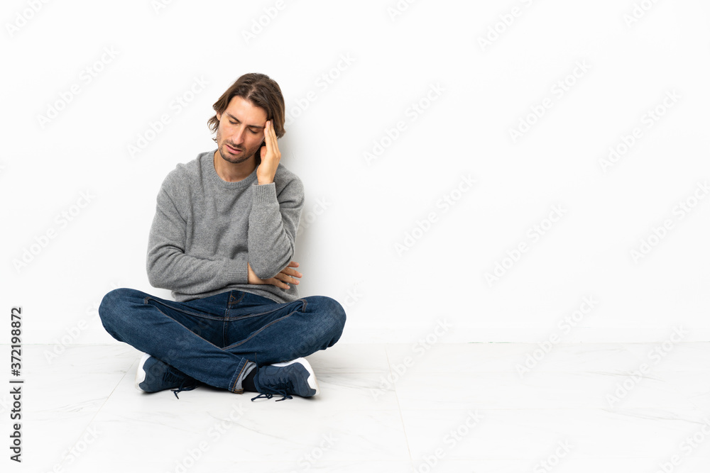 Young handsome man sitting on the floor over isolated background with headache Young handsome man sitting on the floor over isolated background with headache