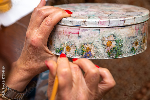 In the woman's hand is a jewelry box on which she makes a decoupage. Handwork.