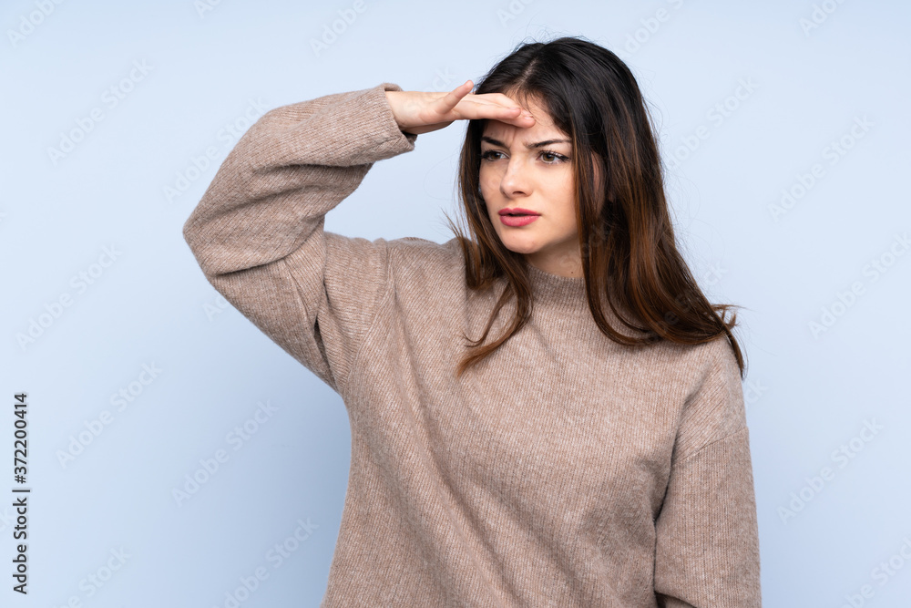 Young brunette woman wearing a sweater over isolated blue background looking far away with hand to look something Young brunette woman wearing a sweater over isolated blue background looking far away with hand to look something
