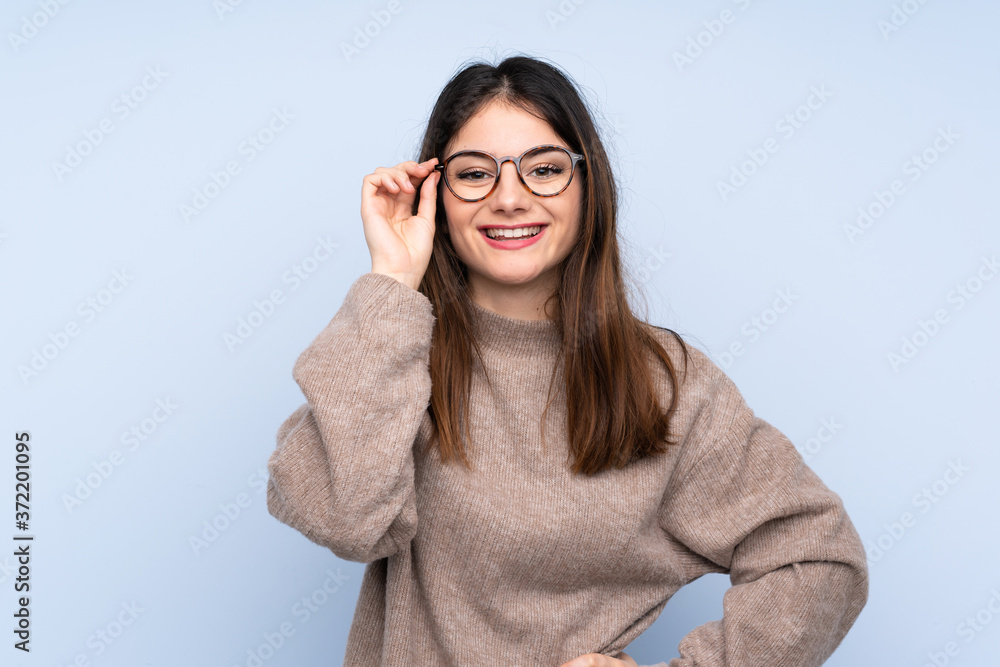 Young brunette woman wearing a sweater over isolated blue background with glasses and happy