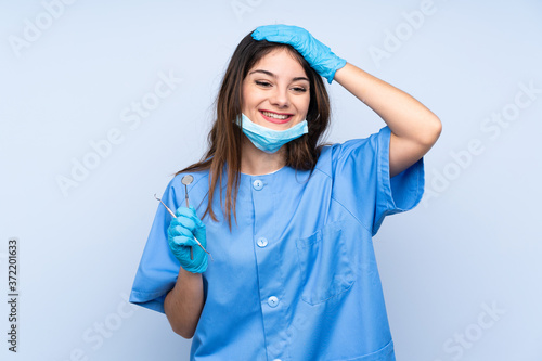 Woman dentist holding tools over isolated blue background laughing