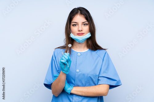 Woman dentist holding tools over isolated blue background keeping arms crossed
