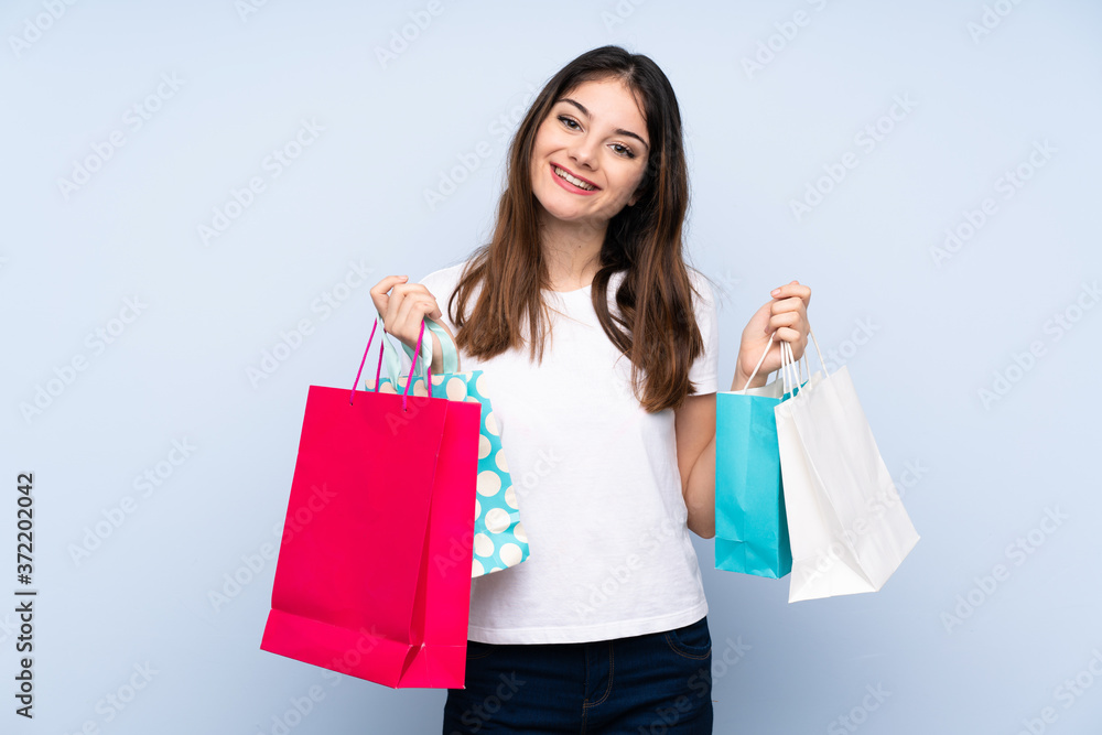 Young brunette woman over isolated blue background holding shopping bags and smiling Young brunette woman over isolated blue background holding shopping bags and smiling