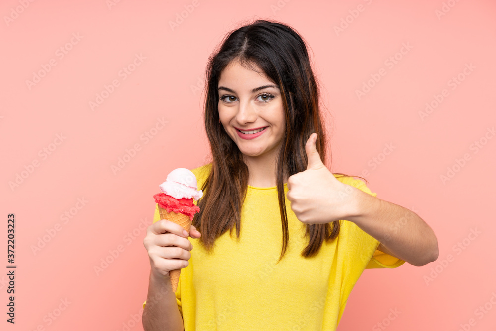 Young brunette woman holding a cornet ice cream over isolated pink background with thumbs up because something good has happened Young brunette woman holding a cornet ice cream over isolated pink background with thumbs up because something good has happened