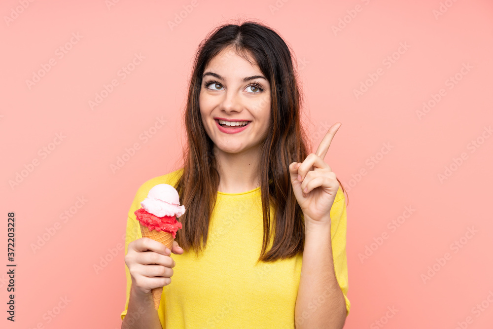 Young brunette woman holding a cornet ice cream over isolated pink background intending to realizes the solution while lifting a finger up Young brunette woman holding a cornet ice cream over isolated pink background intending to realizes the solution while lifting a finger up
