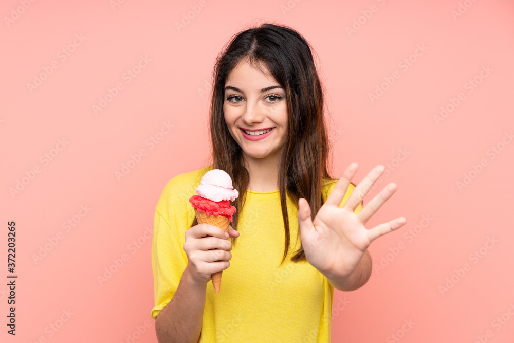Young brunette woman holding a cornet ice cream over isolated pink background saluting with hand with happy expression Young brunette woman holding a cornet ice cream over isolated pink background saluting with hand with happy expression