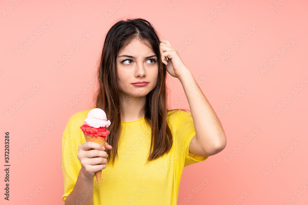 Young brunette woman holding a cornet ice cream over isolated pink background having doubts and with confuse face expression Young brunette woman holding a cornet ice cream over isolated pink background having doubts and with confuse face expression