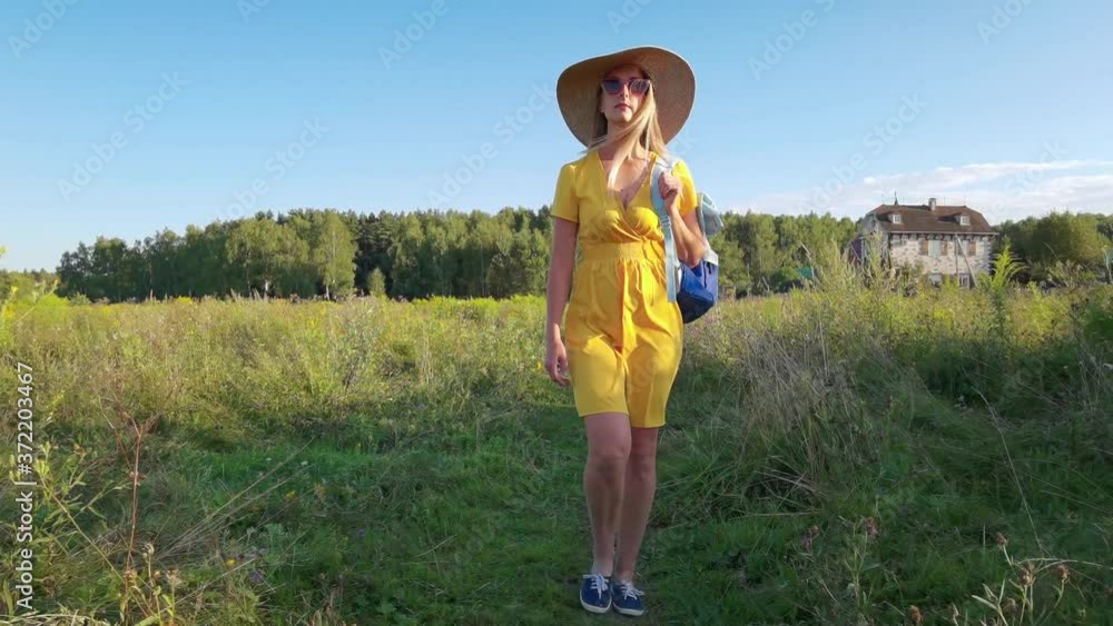 Woman traveler in yellow dress with backpack walking at meadow Woman traveler in yellow dress with backpack walking at meadow